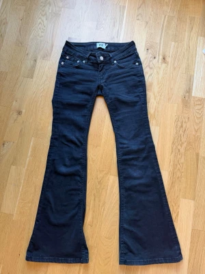Svarta bootcut jeans med låg midja (Blaze)  - Säljer ett par svarta bootcut jeans med låg midja och fem fickor. Jeansen har utsvängda ben och klassisk knappgylf. Dessa par är i short! 