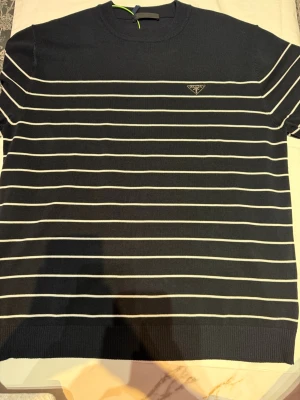 Svart randig kortärmad topp - Snygg svart topp med vita horisontella ränder och rund hals. Kortärmad modell med diskret logga på bröstet. Perfekt till jeans eller kjol för en clean och stilren look.