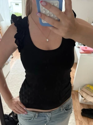 Svart ärmlös topp med volang - Snygg svart topp i ärmlös modell med volangdetaljer på axlarna. Aldrig används⭐️