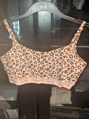 Leopardmönstrad bralette Calvin Klein - Säljer en snygg leopardmönstrad bralette från Calvin Klein med bred resår där det står 'CK ONE CALVIN KLEIN'. Ljusrosa botten med svarta och beige fläckar. Mjuk och stretchig modell utan byglar. Endast testad 1 gång. Inga synliga fläckar eller defekter. Skapa en bundle för bättre pris