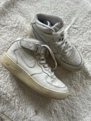 Vita höga sneakers med kardborre - Snygga vita höga sneakers i läder med klassisk snörning och kardborreband vid ankeln. Skorna har perforerad tå, vit sula och diskreta detaljer. Perfekta för dig som gillar en clean och sportig stil.