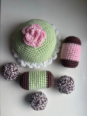 Virkade bakverk i pastellfärger - Säljer ett set virkade bakverk som föreställer prinsesstårta, dammsugare och chokladbollar. Bakverken är gjorda i garn i färgerna ljusgrön, rosa, brun och vit. Perfekt som leksak eller dekoration till köket eller caféhörnan.