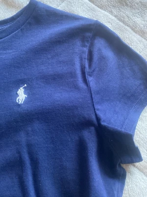 Marinblå t-shirt från Polo Ralph Lauren - Klassisk marinblå t-shirt från Polo Ralph Lauren med den ikoniska vita logobrodyr på bröstet. T-shirten har rund halsringning och korta ärmar. Tillverkad i mjuk bomull som känns skön mot huden. Perfekt för en clean och stilren look. PRIS KAN DISKUTERAS💙