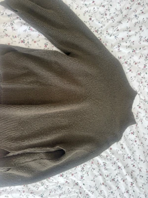 Olivgrön stickad tröja  - Mysig olivgrön stickad tröja med hög hals och ribbade muddar. Tröjan har en avslappnad passform och är perfekt för kyliga dagar. Materialet känns mjukt och värmande, och färgen är lätt att matcha med olika outfits.