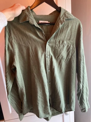  linneskjorta - Snygg olivgrön skjorta från Dressmann i 100% linne. Skjortan har klassisk krage, bröstficka och knäppning framtill. Perfekt för dig som gillar en avslappnad men stilren look. Passar till både jeans och chinos. Strl:M