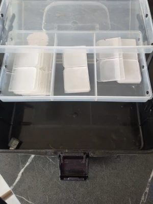 Transparent plastväska med fack - Praktisk transparent plastväska med flera fack och svart handtag. Perfekt för att organisera småsaker eller accessoarer. Väskan har ett klistermärke på locket och tydliga fack för enkel sortering.