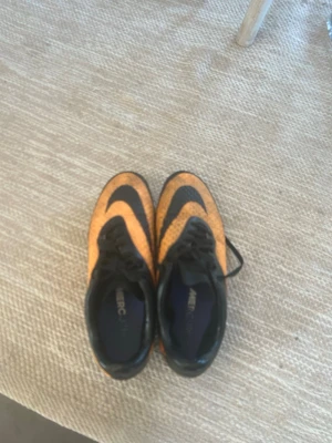Orangea och svarta Nike fotbollsskor - Säljer ett par snygga fotbollsskor från Nike hyper vemoms i storlek 42 som är orange och svarta. Skorna har klassisk snörning, låg profil och mönstrad ovandel för bra bollkontroll. Sulan har dobbar för spel på gräs. Perfekta för dig som vill sticka ut på planen! Pris kan diskuteras 👌