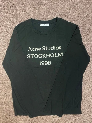 Svart långärmad topp Acne Studios Stl S (oversized) - Svart långärmad topp från Acne Studios med tryck 'Acne Studios STOCKHOLM 1996' i vitt framtill. Klassisk rund halsringning och rak passform. Perfekt för dig som gillar stilrena och tidlösa plagg med en touch av streetwear.
