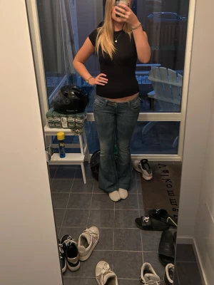 Blå bootcut jeans med stjärndetalj - Säljer ett par blå bootcut jeans med snygg stjärndetalj på ena bakfickan och slitna detaljer vid fickorna. Jeansen har låg midja och klassisk femficksdesign. Perfekta för dig som gillar en avslappnad men trendig look.