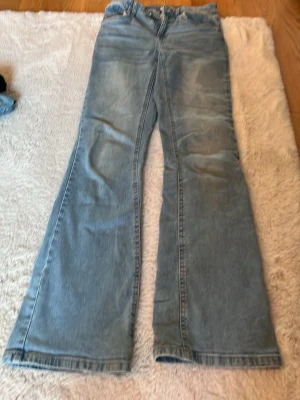 Ljusblå bootcut jeans - Säljer ett par ljusblå jeans med bootcut passform och klassisk femficksdesign. Jeansen har hög midja och är tillverkade i denim med lätt tvättad look. Perfekta för en avslappnad och trendig stil.