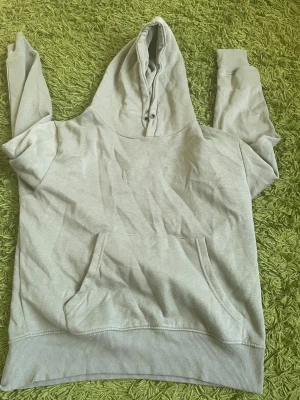 Ljusgrå hoodie med magficka - En enkel och stilren ljusgrå hoodie med stor huva och magficka framtill. Hoodien har ribbade muddar vid ärmslut och nederkant. Perfekt för en avslappnad look och passar till det mesta. Materialet känns mjukt och bekvämt.