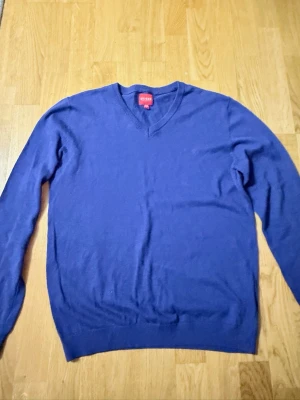 Blå stickad tröja från Guess - Snygg blå stickad tröja från Guess med V-ringning och ribbade muddar vid ärmslut och nederkant. Perfekt för lager på lager och enkel att matcha med jeans eller chinos. Tillverkad i mjukt material som känns skönt mot huden. Tröjan sitter perfekt. Tröjan är använd ett par få gånger 