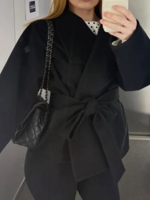 Kort svart kappa med knytskärp -  Kort svart kappa med knytskärp i midjan. 