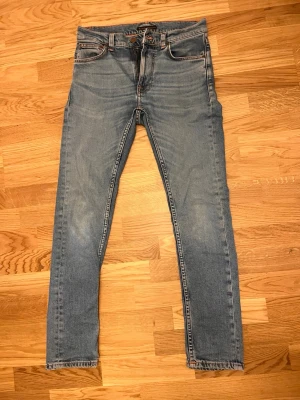 Nudie Jeans Lean Dean  - Säljer ett par ljusblå slim fit jeans med klassisk femficksdesign och råa benslut. Jeansen har en snygg tvätt och kontrastsömmar, samt detaljerade bakfickor. Perfekta för en avslappnad och trendig look.