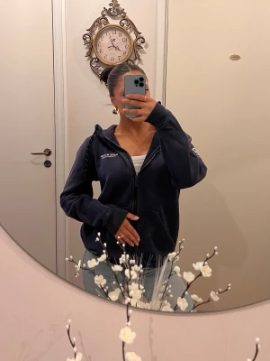 Mörkblå zip hoodie med tryck - Snygg mörkblå hoodie med dragkedja och huva. Tryck med siffran 83 och texten 'RACE MARINE' på ena ärmen. Mjukt material och ribbade muddar vid ärmslut och nederkant. Perfekt för en avslappnad och sportig look.