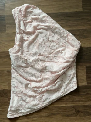 Ljusrosa spets asymetrisk topp från Gina - Snygg ljusrosa topp med spetsdetaljer och blommigt mönster. Den är oneshoulder och går att ha åt båda håll så man kan täcka vilken axel man vill. Inte genomskinlig och har dubbla lager. Använd fåtal gånger och i bra skick. Kom gärna med prisförslag!💗