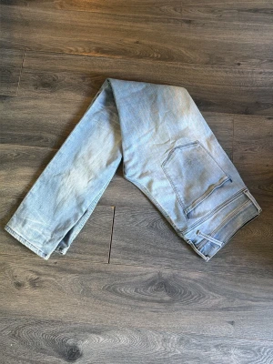 Replay jeans - Säljer ett par ljusblå replay jeans med slitningar på ena benet. Jeansen har klassisk femficksdesign och är tillverkade i stretchigt denimtyg för en bekväm passform. Perfekta för en avslappnad och trendig look.