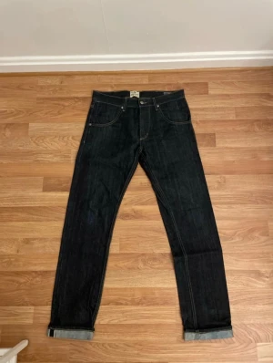 Vintage Wrangler Blue Bell Eddy Beverly Dry Selvedge Jeans - W31 L34 Made in USA Raw Denim Aldrig använda eller tvättade. Dem är i utmärkt skick och gjorda cirka sent 90 eller tidigt 2000 tal. Modellen är Wrangler Blue Bell Eddy Beverly Dry jeans. Premium Made in USA selvedge denim i classic straight/skinny/Cowboy Cut fit. Priset är inte hugget i sten så buda om ni vill!