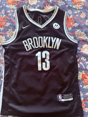 Brooklyn Nets basketlinne #13 James Harden  - Snyggt svart basketlinne med BROOKLYN och nummer 13 på framsidan samt HARDEN och nummer 13 på baksidan. Linnet har vita detaljer längs kanterna och ärmlöst snitt. Perfekt för basketträning eller att bära som streetwear.