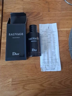 Dior Sauvage Eau de Parfum 100Ml - Dior Sauvage Eau de Parfum är en elegant herrdoft i en mörkblå, cylinderformad glasflaska med vit text. Flaskan har en stilren och modern design och kommer med originalkartong. En ikonisk parfym som ger ett fräscht och maskulint intryck. Den är ny med öppnad förpackning