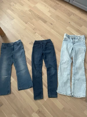 Tre par jeans i olika blå nyanser - Säljer tre par jeans i olika blå tvättar. Ett par är ljusblå med raka ben, ett par är mörkblå med smal passform och resår i midjan, och ett par är mellanblå med lätt utsvängda ben. Alla har klassisk femficksdesign och är tillverkade i denim.