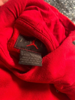 Röd hoodie från Jordan med logga - Snygg röd hoodie från Jordan med klassisk Jumpman-logga på bröstet. Hoodien har huva och en stor magficka framtill. Tillverkad i mjukt material som känns skönt mot huden. Perfekt för dig som gillar streetwear och sportig stil.