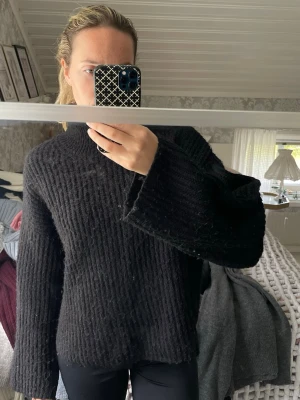 Svart stickad tröja - Svart stickad tröja med ribbad struktur och hög hals. Tröjan har långa, vida ärmar och en relaxed passform. 