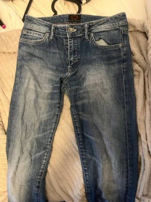 Blå slitna jeans med utsvängda ben - Säljer ett par blå jeans från Crocker med snyggt slitna detaljer och utsvängda ben. (dom var straight innan men sydde om dom med mörkare tyg som en snygg detalj) Jeansen har en rosa detalj, normal-low midja och ljusare tvätt på låren. Perfekta för en avslappnad och trendig look.