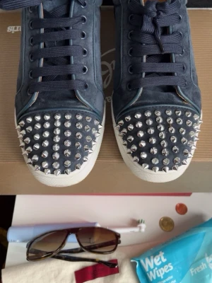 Christian Louboutin Mörkblå Sneakers med Nitar – Storlek 39 - Säljer ett par mörkblå sneakers med coola silverfärgade nitar över hela tån. Skorna har vita sulor och matchande mörkblå skosnören. Materialet ser ut att vara mocka eller liknande och designen är riktigt edgy och unik kan tvätta innan jag skickar och pris kan diskuteras vid snabbaffär