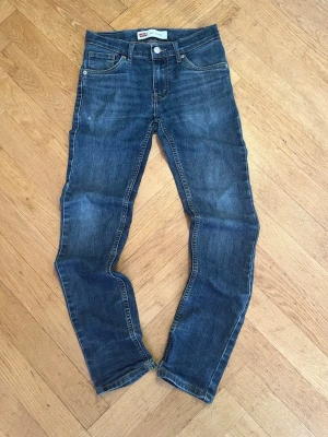 Levis jeans 510tm skinny - Säljer ett par fina Levi's 510™ Skinny jeans i en klassisk mörkblå denimtvätt.Modell: 510™ Skinny FitStorlek: 152 cm (motsvarar ca 12 år / 12A)Skick: Bra begagnat skick. Det finns ett litet ytligt skraphål/nöthål på tyget (se sista bilden), men i övrigt är de hela och fina.Detaljer: Klassisk femficksmodell med stretch som gör dem superbekväma. Justerbar resår finns i midjan för perfekt passform.Perfekta jeans till både vardag och skola!