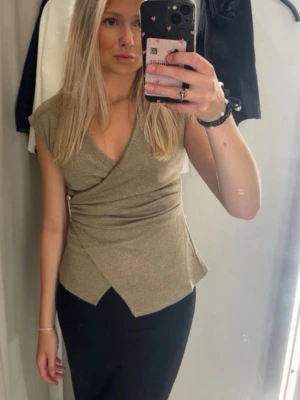 Beige omlottopp med v-ringning - Snygg beige omlottopp med v-ringning och korta ärmar. Toppen har en figurnära passform och ett omlott-detalj framtill som ger en cool look. 