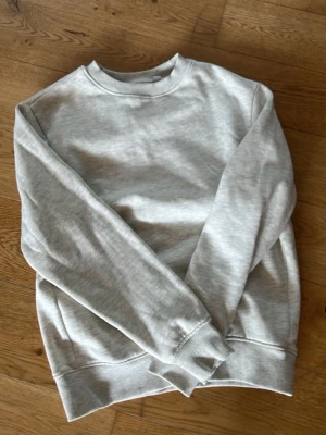 Ljusgrå sweatshirt - En enkel och stilren ljusgrå sweatshirt med rund hals och långa ärmar. Tillverkad i mjuk bomull för maximal komfort. Perfekt basplagg att matcha med jeans eller kjol.