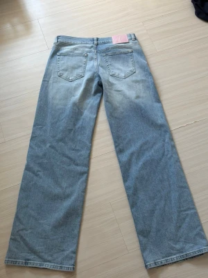 Ljusblåa raka jeans med vida ben - Nypris 699. Storlek 38. Säljer ett par ljusblå jeans med raka, vida ben och klassisk femficksmodell. Jeansen har en avslappnad passform och subtila slitningar framtill för en cool vintagekänsla. Perfekta till sneakers eller boots för en trendig look. 
