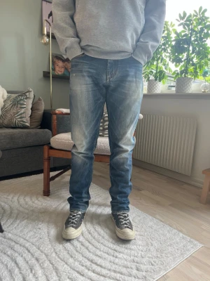 Tommy Hilfiger Denim Jeans W31 L32 Blå Denim - Hilfiger Denim jeans i klassisk blå tvätt med naturligt slitage. Rak/reguljär passform genom benet, klassisk femficksmodell med läderlapp bak och Hilfiger-flagga på fickan.  Skick: bra skick, inga hål eller fläckar Material: denim (se innertagg för exakt materialmix) Midja: W31 Innerbenslängd: L32 Modell: 175 cm / 65 kg 