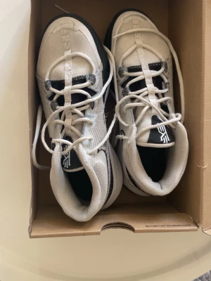 Kyrie Nike Flytrap basketsskor Limited Edition - Säljer ett par vita Nike Kyrie basketsskor med svart och gråa detaljer. Skorna har mesh-ovandel för bra ventilation, klassisk snörning och en stabil sula som passar perfekt för basketplanen. Snygg design med Kyrie-logga på plösen. Dessa skor går inte att köpa längre pågrund av att kyrie inte samarbetar med Nike.