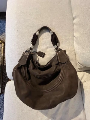 Dkny 2000-tals väska - Brun vintage DKNY bag från 2000-talet i modellen hobo. Den är i mjukt brunt äkta läder och är i bra skick. Modellen är en härlig, avslappnad slouchy look. Märket sitter diskret på sidan av väskan. Den är stor och har bra förvaring på insidan, perfekt om man går i skolan och vill ha plats för dator och olika böcker. Pris kan diskuteras och om du har frågor skriv gärna!💗