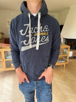 Jack&Jones vintage hoodie med broderat tryck blå herr - Mörkblå hoodie från Jack & Jones med snyggt broderat Originals-tryck framtill. Vit huva och snören som ger en klassisk look. Känguruficka och ribbade muddar. Stilren och lättmatchad.  #jackandjones #hoodie #originals #menswear #streetwear #navy #darkblue #casual #sweatshirt #retro #fashion