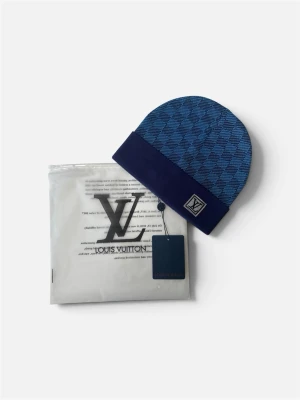 Blå stickad mössa med rutigt mönster – helt ny 💙 -  mössa i en fin blå nyans med klassiskt rutigt mönster och en mörkblå vik. Tillverkad i mjuk och värmande kvalitet som passar perfekt under kalla dagar. Helt oanvänd med etikett kvar och levereras i originalförpackning. En elegant accessoar som lyfter vilken vinteroutfit som helst. Välkommen att kontakta oss vid frågor. 🧣✨
