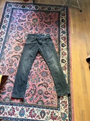 Gråa Replay Rocco - Snygga grå slim fit jeans från Replay med klassisk femficksdesign och diskreta slitningar. Jeansen har normal midja och raka ben, perfekta för en avslappnad men ändå stilren look. Materialet är mjukt denim som ger bra komfort.