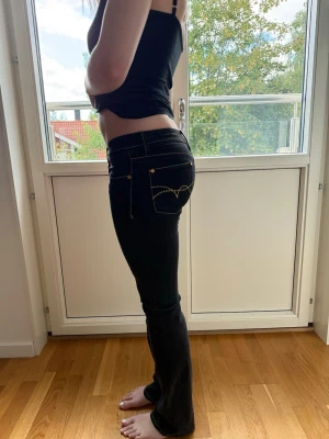 Svarta lågmidjade jeans med kontrastsömmar - Säljer ett par svarta jeans med låg midja och raka ben. Jeansen har tydliga kontrastsömmar i gult och klassiska fickor både fram och bak. Passformen är normal och materialet är klassisk jeans med stretch.