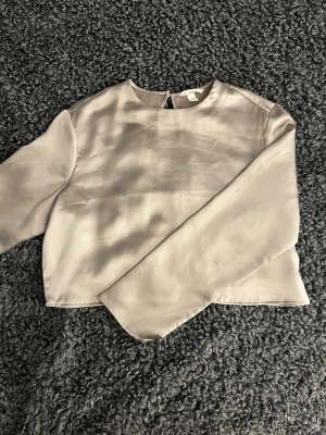 Ljuslila satinblus med lång ärm - Snygg ljuslila blus i satin med rund halsringning och långa ärmar. Blusen har en stilren och minimalistisk design med en lätt glansig yta som ger en lyxig känsla. Perfekt att styla med jeans eller kjol för en trendig look.
