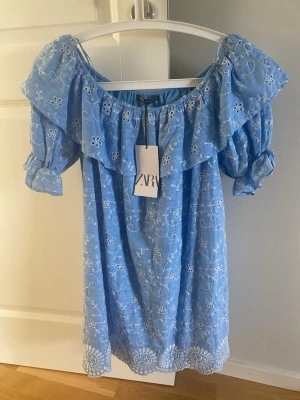 klänning från Zara - Söt blå kortklänning från Zara med vita broderade blommor, volang vid axlarna och korta puffärmar. Klänningen har offshoulder-design och är perfekt för varma dagar. Tillverkad i bomull för en luftig och bekväm känsla. ALDRIG ANVÄND PRIS KAN DISKUTERAS❤️❤️