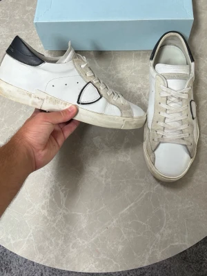Philippe model skor - Säljer ett par vita Philippe model sneakers med svarta detaljer och beige partier. Skorna har klassisk snörning och en låg profil. Tillverkade i skinn och mocka för en schysst mix av material. Box medföljer ej. Dessa skor är sjukt trendiga just nu och passar perfekt för dig som gillar stilrena men ändå unika sneakers. Skorna är i mycket bra skick och har knappt använts.