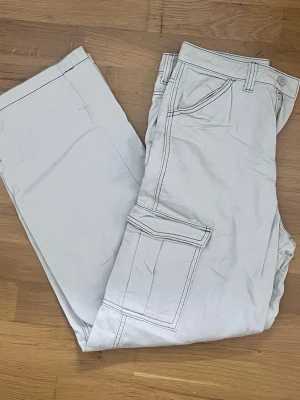 Ljusa cargobyxor från Divided H&M - Säljer ett par ljusa cargobyxor från Divided H&M i storlek 36. Byxorna har klassiska cargofickor på sidorna, raka ben och bälteshällor. Tillverkade i ett mjukt bomullstyg som är bekvämt att bära. Perfekta för en avslappnad och trendig look.