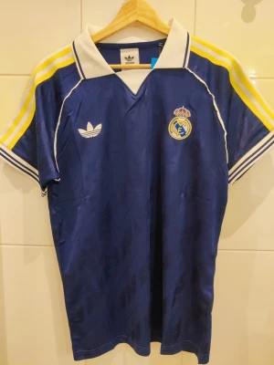 Real Madrid retro fotbollströja  - Säljer en retro Real Madrid fotbollströja i marinblå färg. Tröjan är en reprint helt ny och oanvänd. Storlek M.