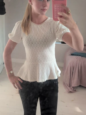 Vit blus med volang och puffärm - Söt vit blus med broderade hål och volang nedtill. Blusen har puffiga korta ärmar och rund halsringning. 