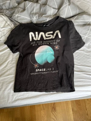 Svart NASA t-shirt med tryck - Väldigt fräsch och fin T-shirt i använt men gott skick, inga fläckar eller liknande på den, jag har använt den några gånger bara. Storlek är XS på den.  POV: om personen som köper den inte bor i närheten av mig kan jag göra ett undantag att skicka den men annars ska den hämtas på plats! 