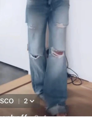 Ljusblåa slitna wide leg jeans - Säljer ett par ljusblåa jeans med bred passform och slitningar vid knäna. Jeansen har hög midja och vida ben, samt råa kanter längst ner. Perfekta för en avslappnad och trendig look.