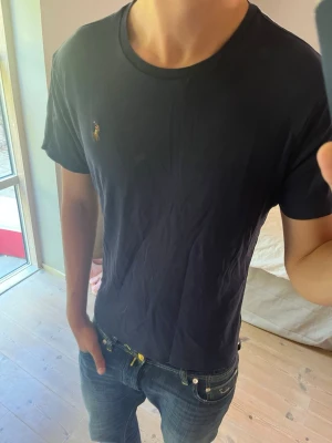 Mörkblå t-shirt från Polo Ralph Lauren - Snygg mörkblå t-shirt från Polo Ralph Lauren med klassisk passform och liten broderad logga på bröstet. Tillverkad i mjuk bomull och har rund halsringning samt korta ärmar. Perfekt till jeans eller shorts för en clean look.