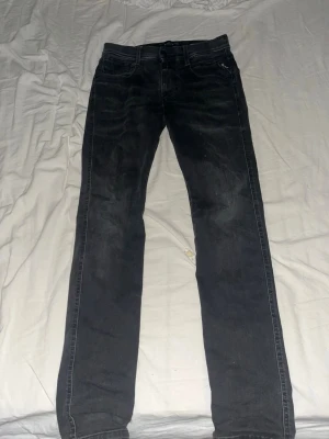 Replay svarta slim fit jeans - Snygga svarta slim fit jeans från Replay med klassisk femficksdesign och diskreta slitningar. Jeansen har normal midja, dragkedjegylf och Replay-logga på fickan. Perfekta för en trendig och avslappnad look.